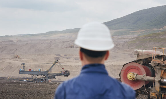 Coal mining in surface mine. Miner looking on the huge excavator.